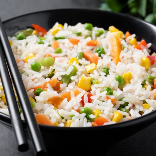 White rice with vegetables in a black bowl on black background